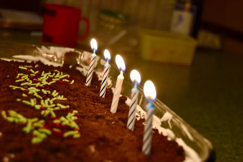 Lit candles on a chocolate birthday cake decorated with green sprinkles