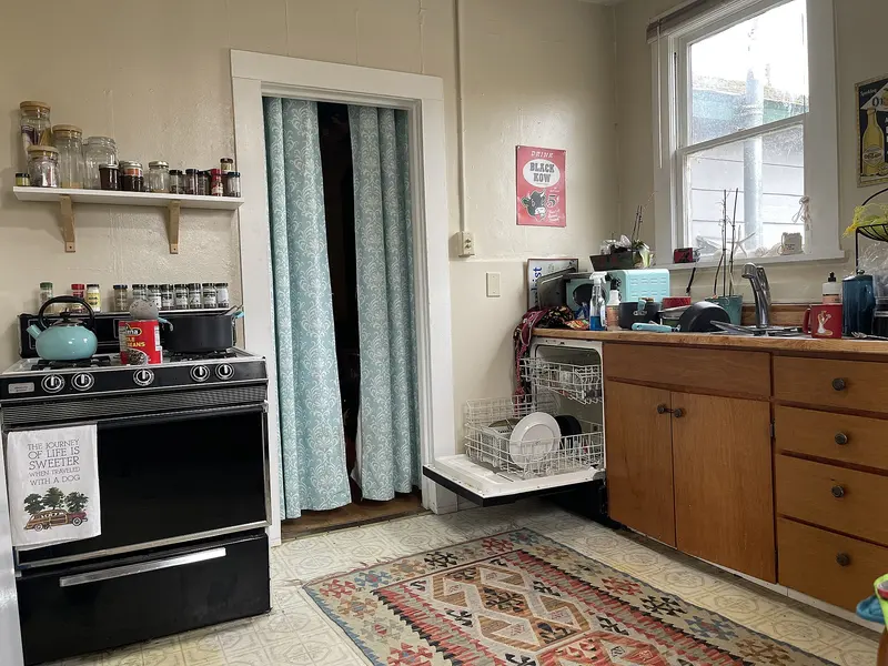 A homely kitchen with open shelves, a cooker, a patterned rug and a sunny window