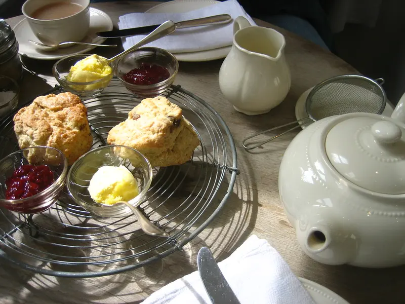 Scones with little dishes of jam and clotted cream beside a white teapot and cups
